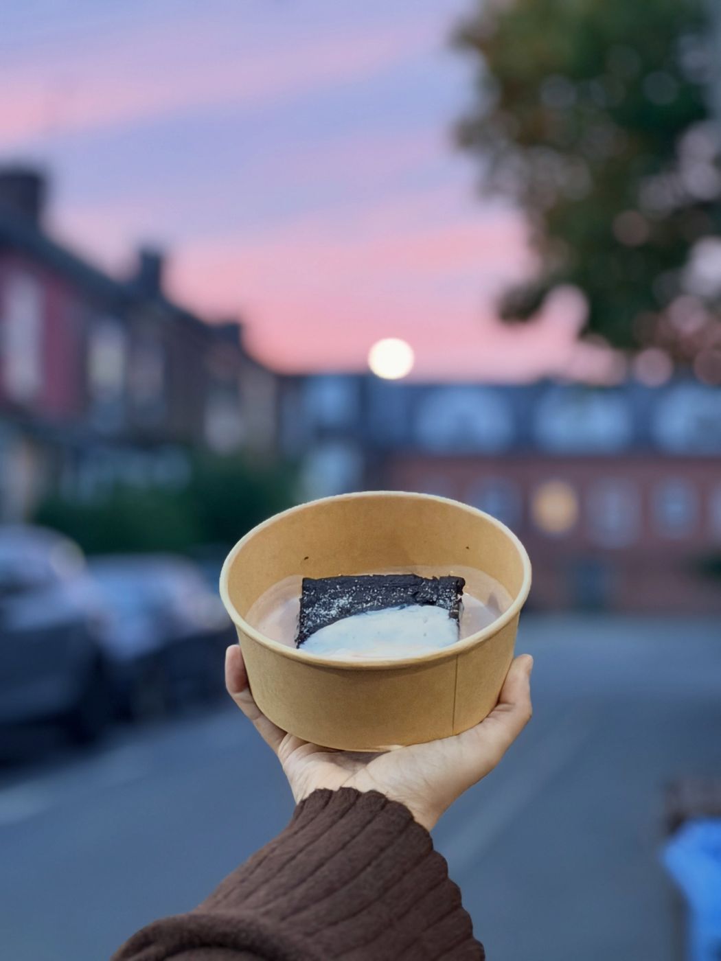 A pot of chocolate concrete with pink custard held up on the street at sunset
